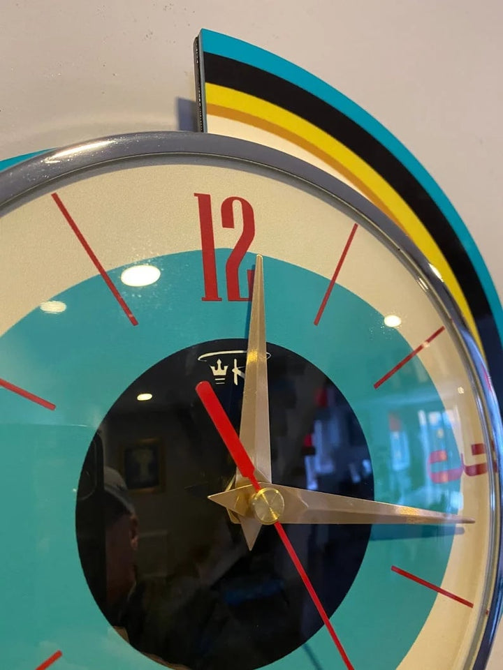 Close-up detail of the swirl wall clock's dial, showing red 12 numeral, gold hands, red second hand, chrome rim and striped backing.