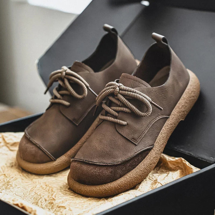 Brown lace-up shoes with suede toe caps presented in an open black box with paper 15