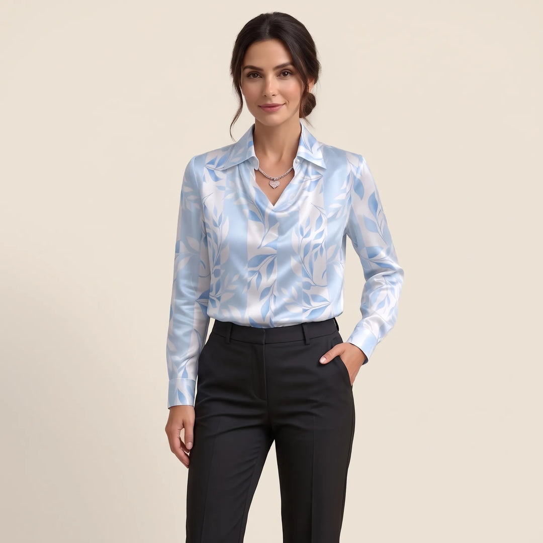 Studio view of the light blue and white leaf-print blouse worn with black trousers, one hand in pocket 15