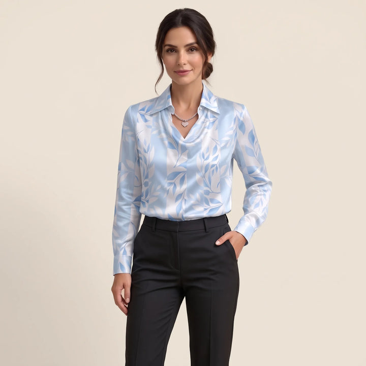 Studio view of the light blue and white leaf-print blouse worn with black trousers, one hand in pocket 15