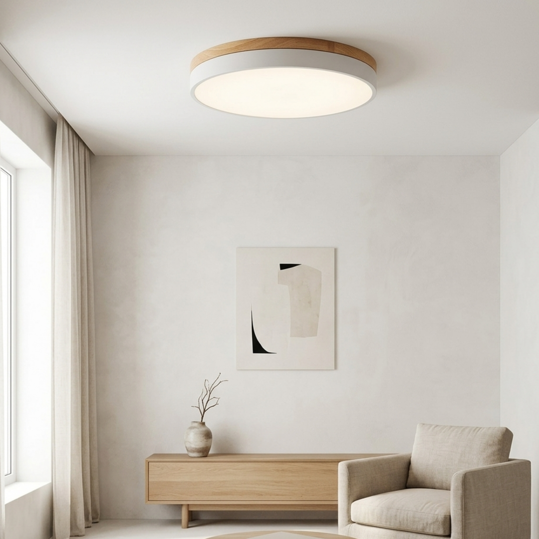White disc ceiling light with a wood-grain top band glowing softly above a minimalist living room with an armchair and sideboard. 3