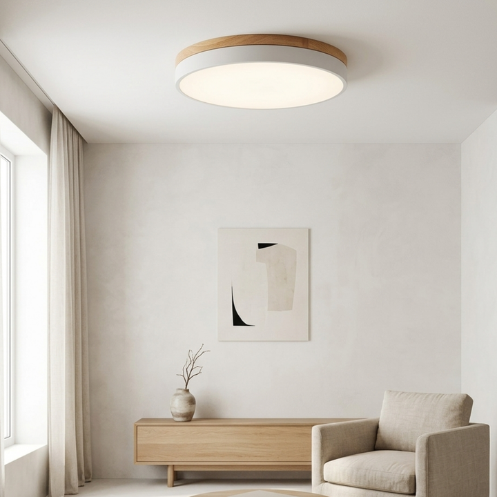 White disc ceiling light with a wood-grain top band glowing softly above a minimalist living room with an armchair and sideboard. 3