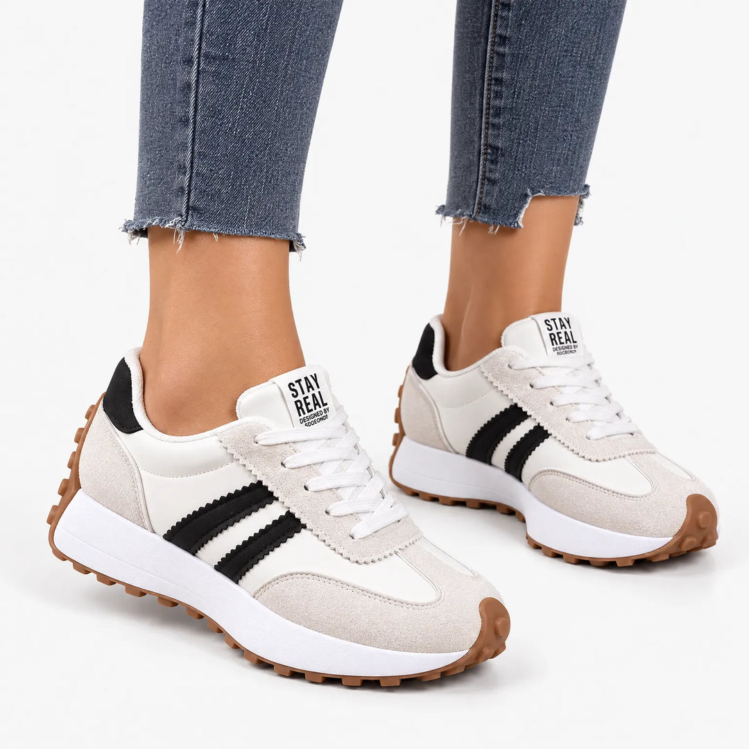 Cream and white platform trainers with black stripes and gum sole, worn with dark jeans on a plain background 15