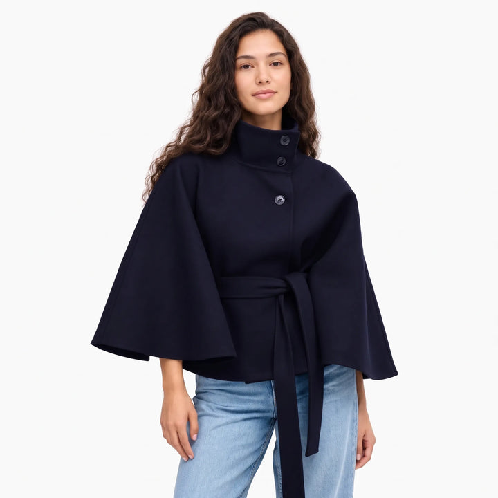 Studio shot of a model in the navy cape jacket with long belt tails and light jeans 15