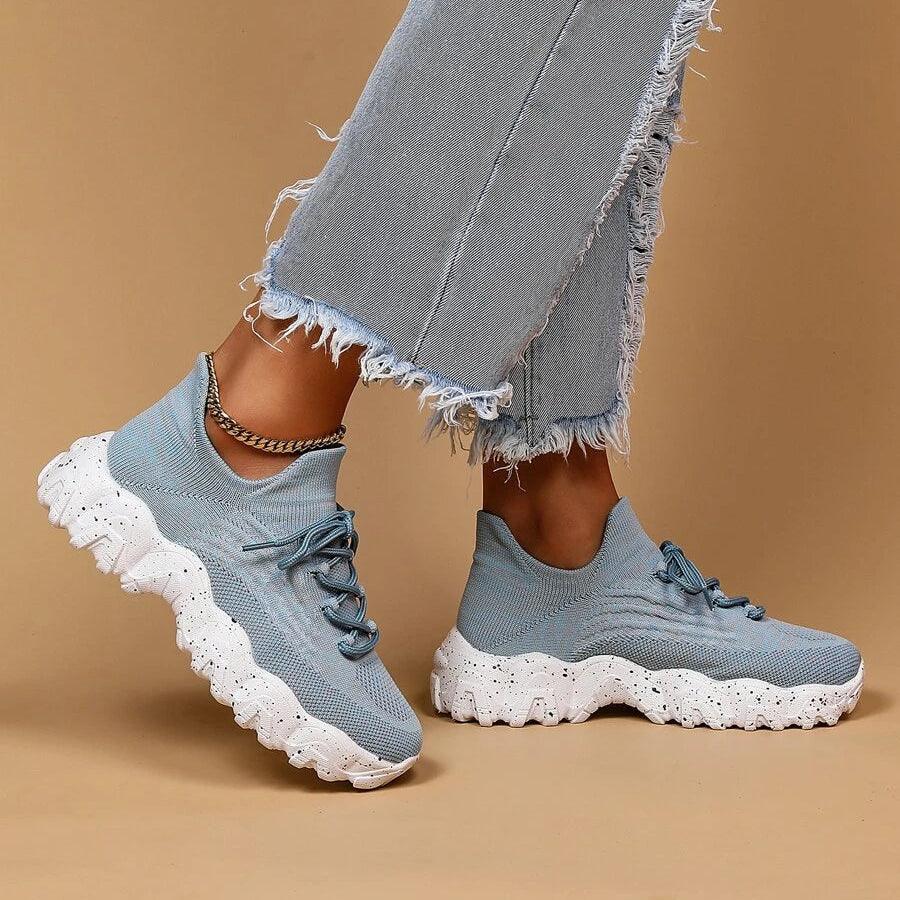 Another view of light blue knit sneakers with chunky white speckled soles, cropped frayed jeans and a gold ankle chain.