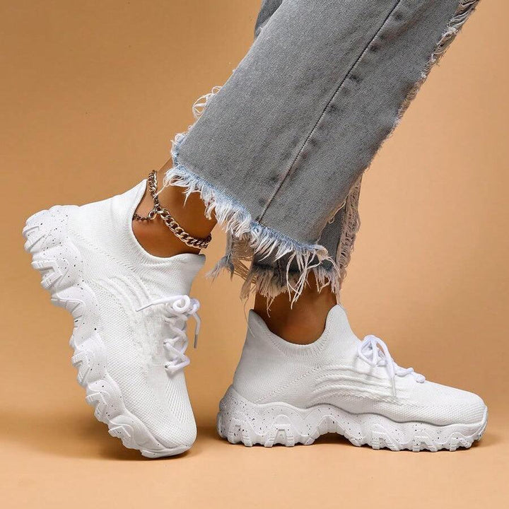 Another view of white knit sneakers and frayed jeans, one foot angled to show the wavy speckled sole.