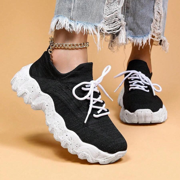 Front three-quarter view of a model in black knit sneakers with white laces and chunky white speckled soles. 36