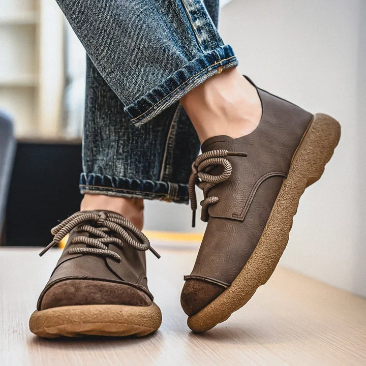 Brown lace-up shoes worn with rolled jeans, one foot lifted to show the sole 16