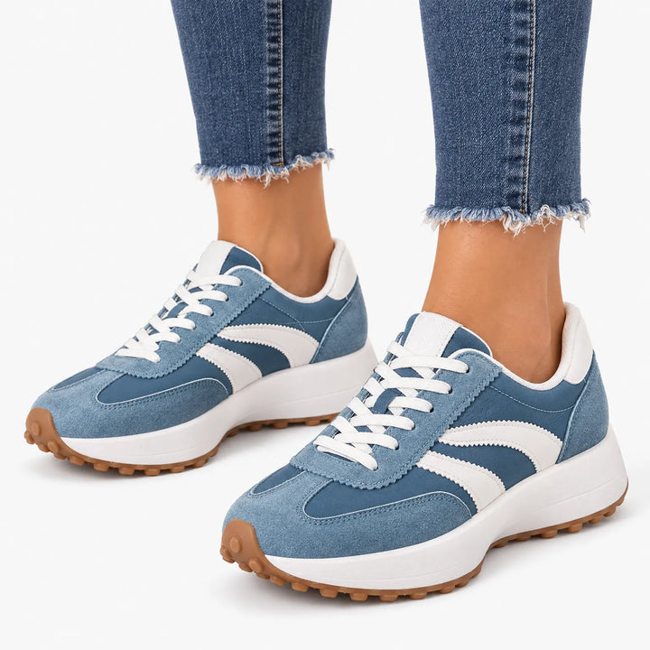 Blue trainers with curved white stripes and white laces, worn with cuffed jeans on a plain white background 16