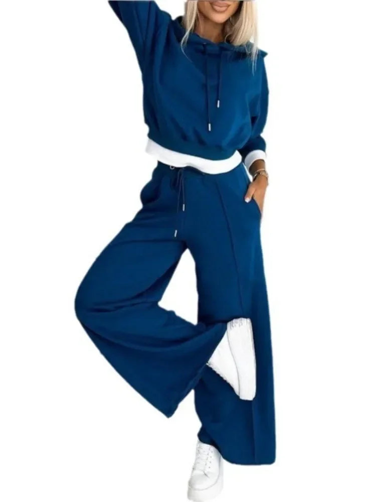 Model in a blue hoodie and wide-leg pants with white trim on a plain white background, one leg raised 16