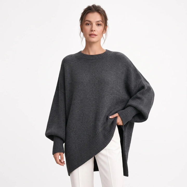 Studio shot of charcoal gray oversized knit sweater with ribbed cuffs, worn with white trousers 16