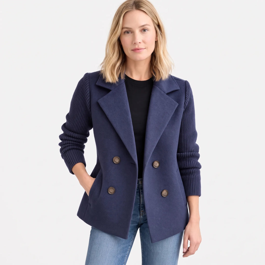 Model in navy jacket with ribbed sleeves, hand in pocket, worn open over black top and jeans 16