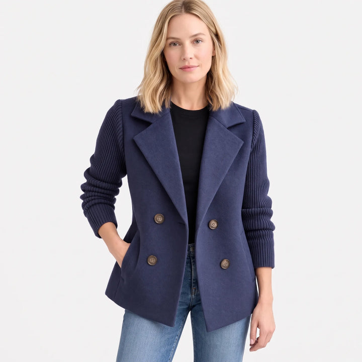 Model in navy jacket with ribbed sleeves, hand in pocket, worn open over black top and jeans 16