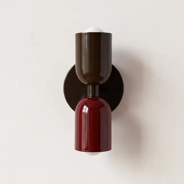 Wall lamp with a dark brown upper shade and glossy burgundy lower shade on a round dark backplate, against a white wall. 24