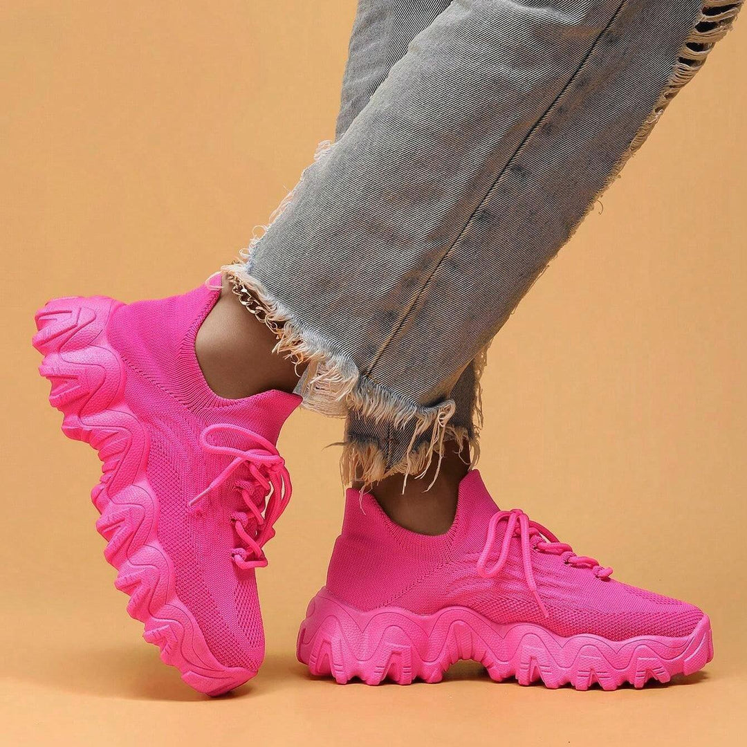 Model in hot pink knit sneakers with one foot lifted, showing the sock-style collar and thick sculpted platform sole. 26