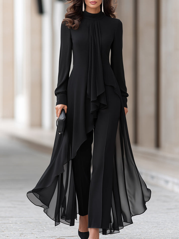 Woman in a black long-sleeve chiffon tunic with draped neck panel over black wide-leg pants, cropped from the face down, holding a clutch. 1