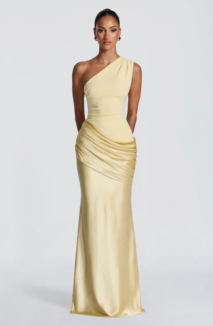 Model in the pale yellow version of the one-shoulder maxi dress, standing straight with arms behind her, shown from the front. 25