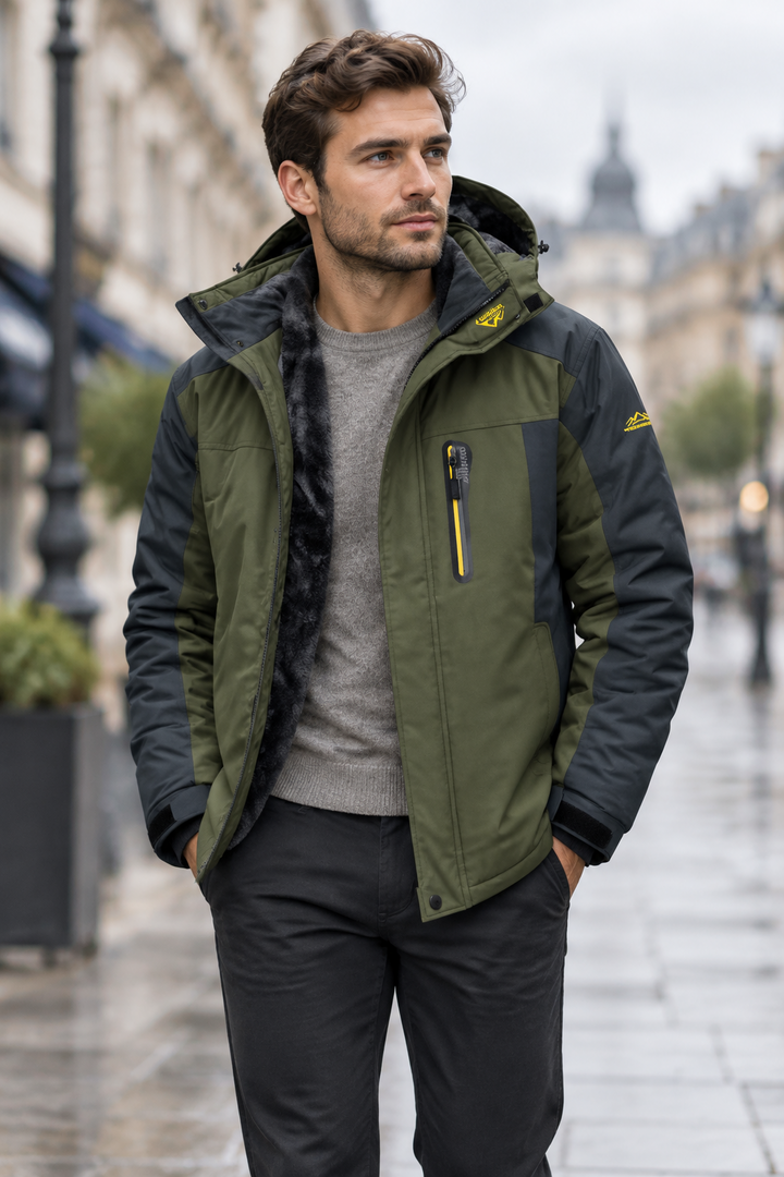 Man in an olive green and charcoal hooded jacket, open over a gray sweater, on a rainy city street 1