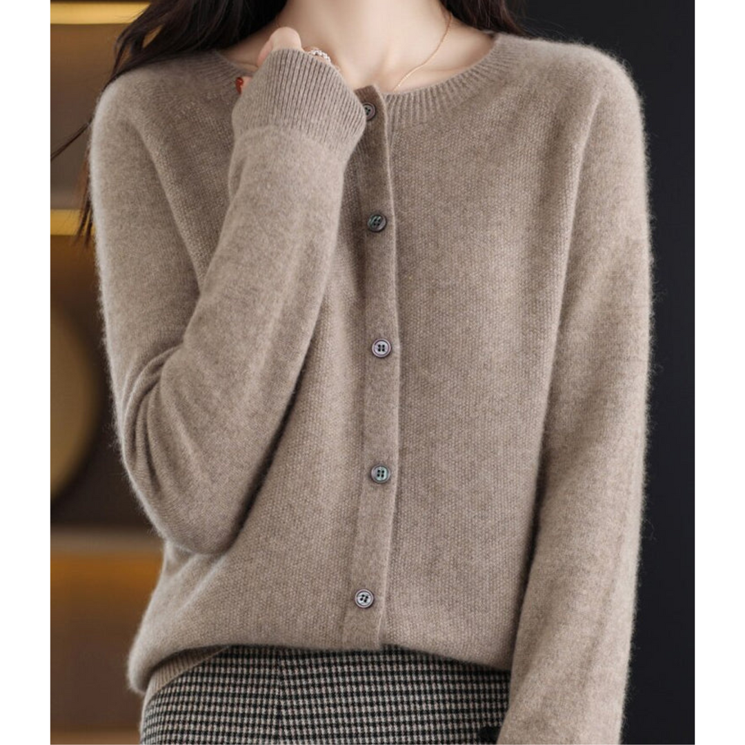 Woman wearing a taupe brown knit cardigan with pearlescent buttons, hand raised to her collar, styled with a houndstooth skirt. 10