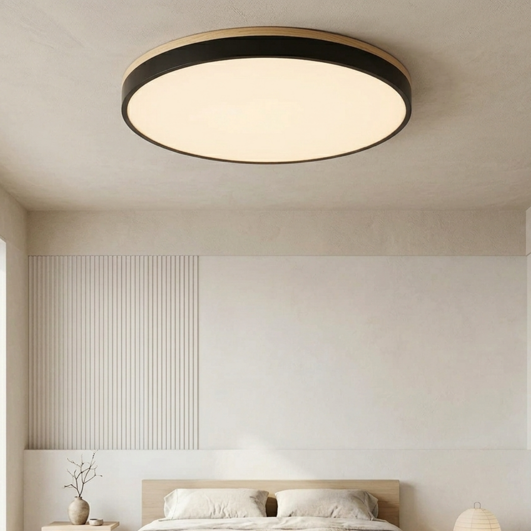 Large black disc ceiling light with a wood-look trim glowing warm white above a bed in a calm neutral bedroom. 2