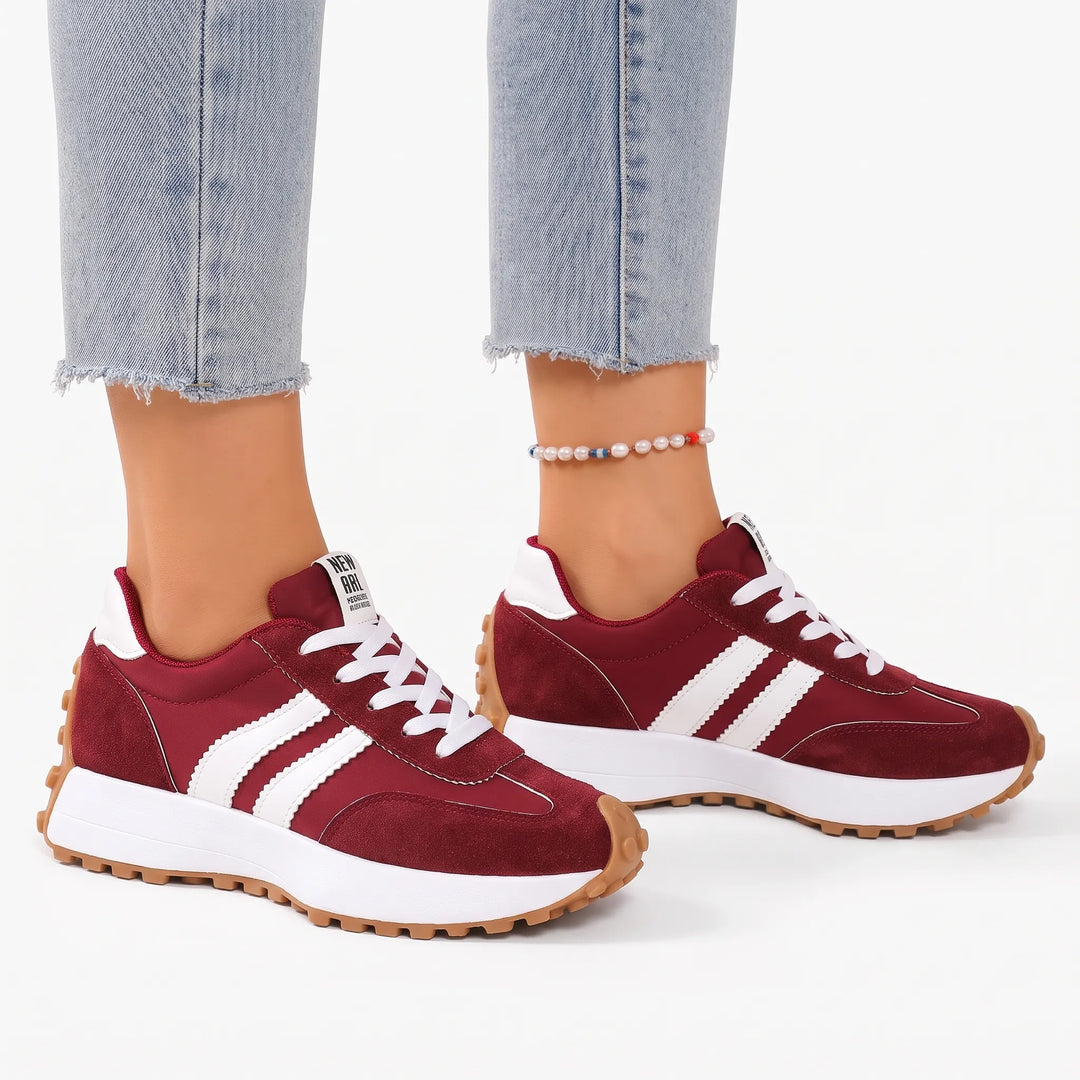 Burgundy platform trainers with white stripes and a studded gum sole, worn with light jeans on a white background 17