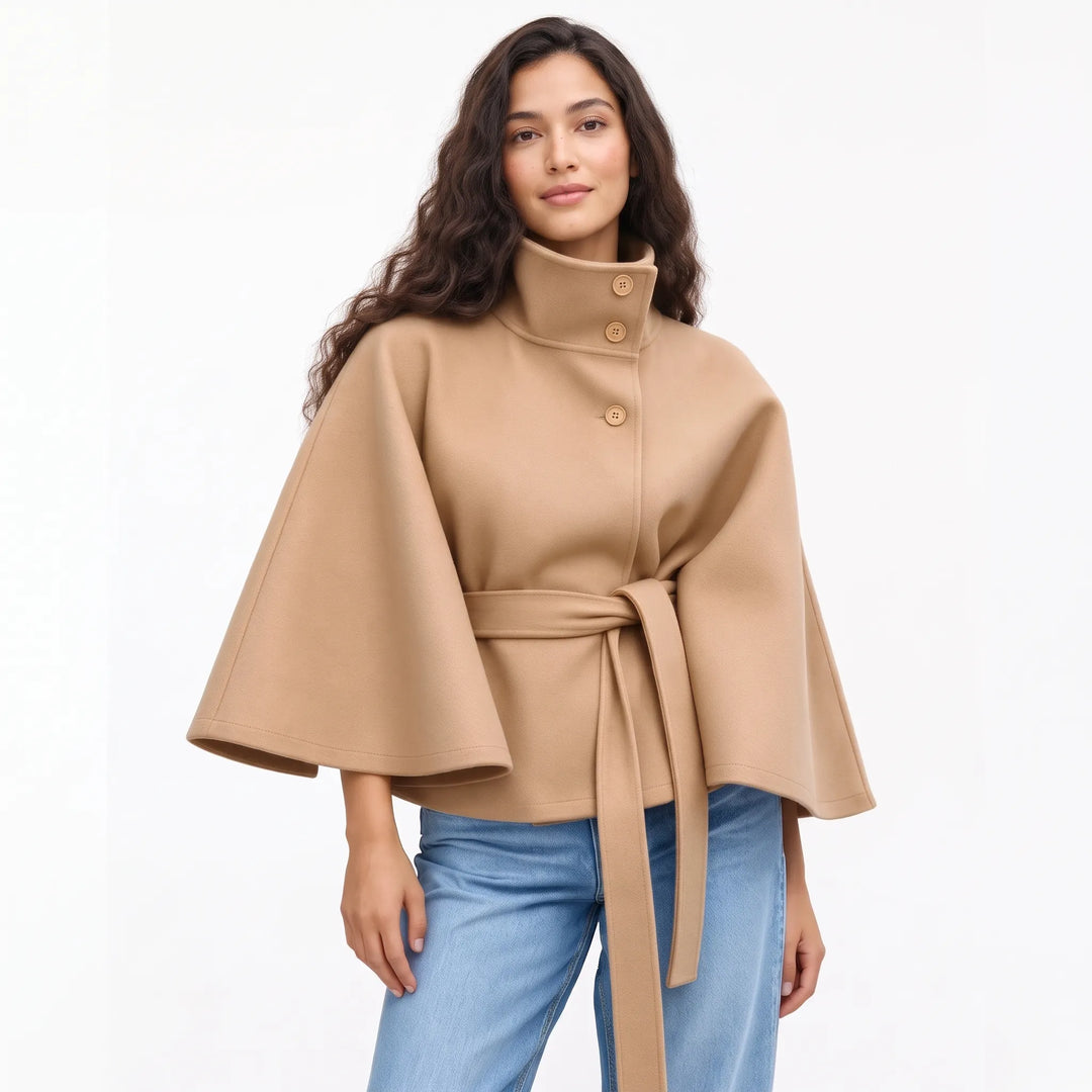 Studio shot of a model in the camel cape jacket with matching buttons and tied belt 18