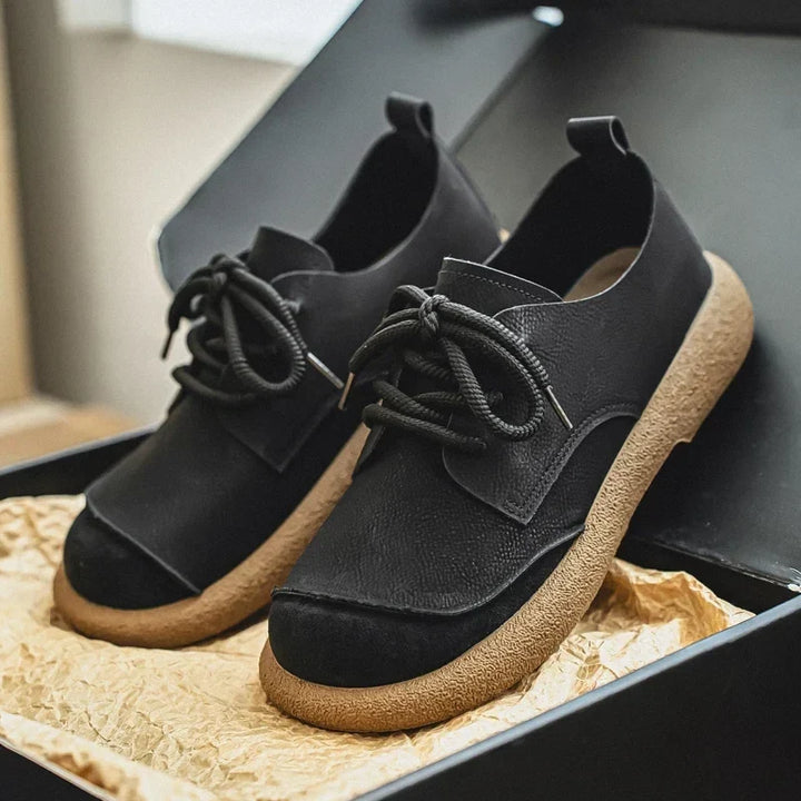 Black lace-up shoes with tan soles displayed in an open box on crinkled paper 18