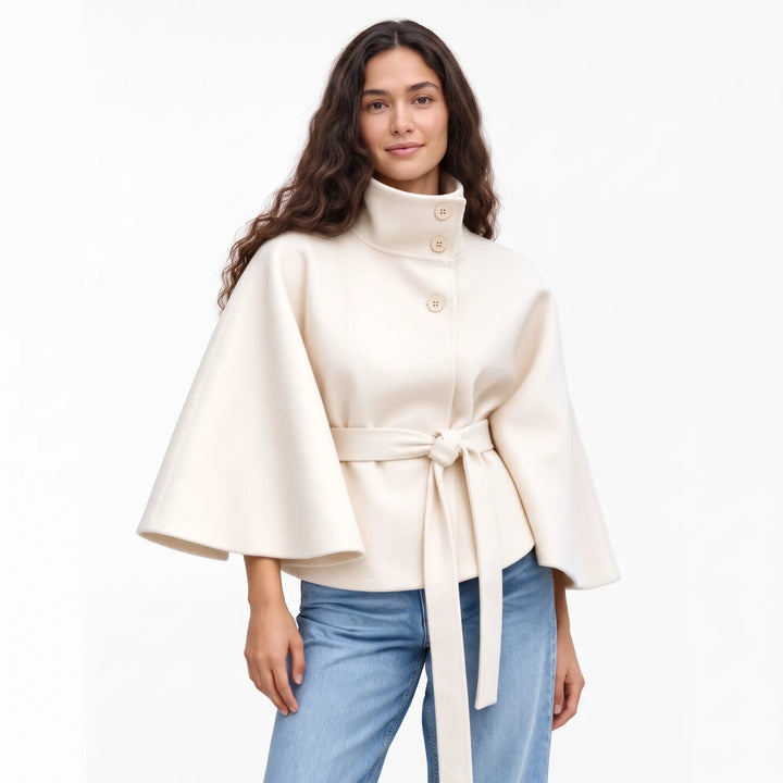 Studio shot of a model in the cream cape jacket with a knotted belt and buttoned collar 19