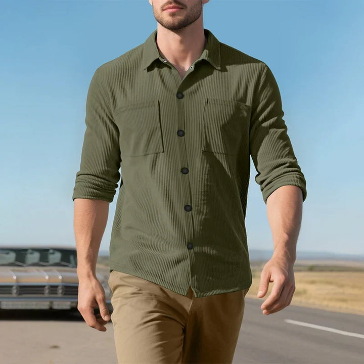 Model walking in the olive green ribbed shirt with rolled sleeves on a road under a blue sky 19