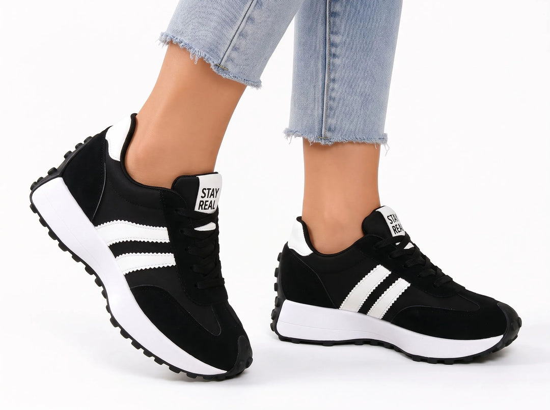 Black platform trainers with white stripes and a chunky white midsole, worn mid-step with light frayed jeans 19