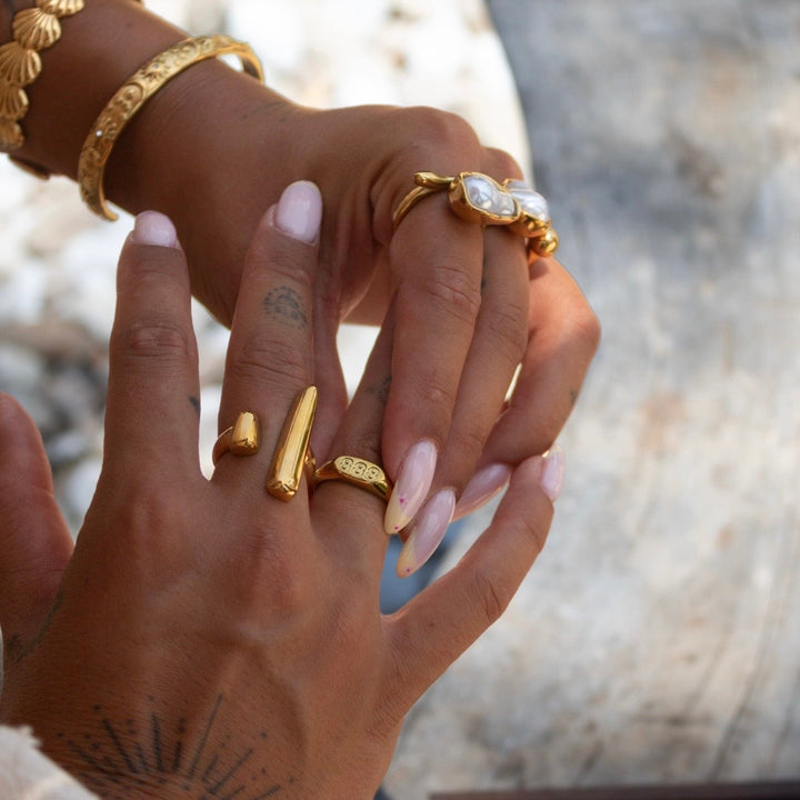 Axis adjustable sculptural gold ring worn on the index finger with nearby rings.