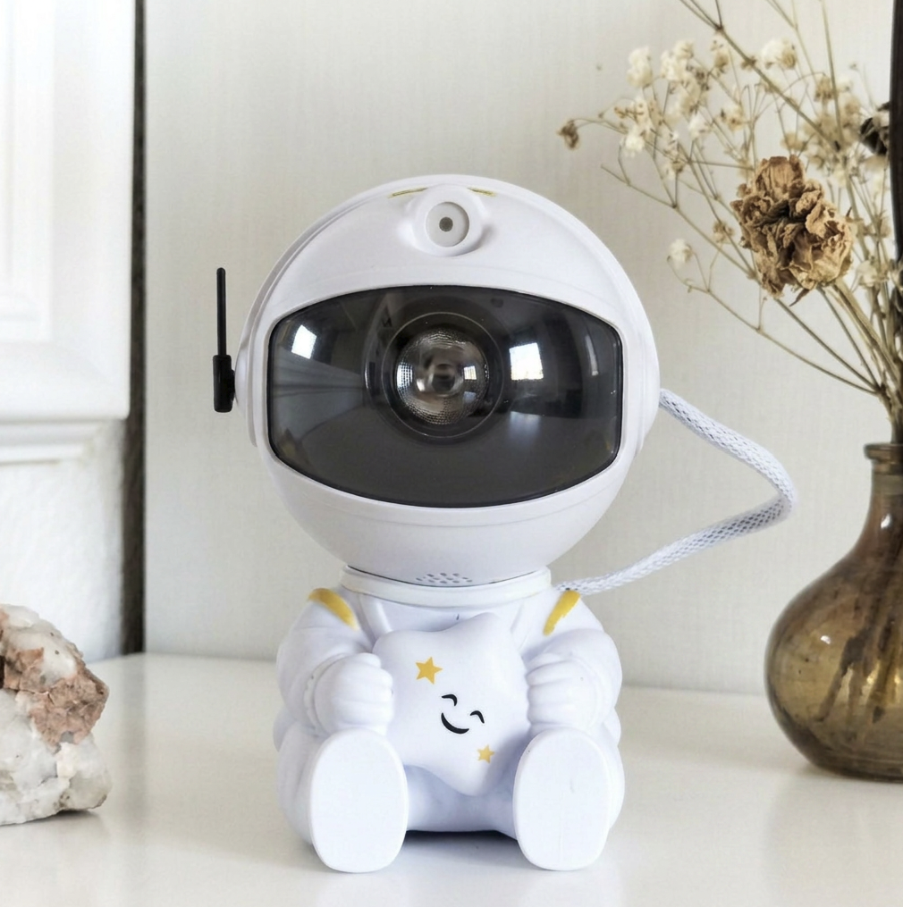 White astronaut projector holding a smiling star, with a white braided cord, on a shelf beside dried flowers.