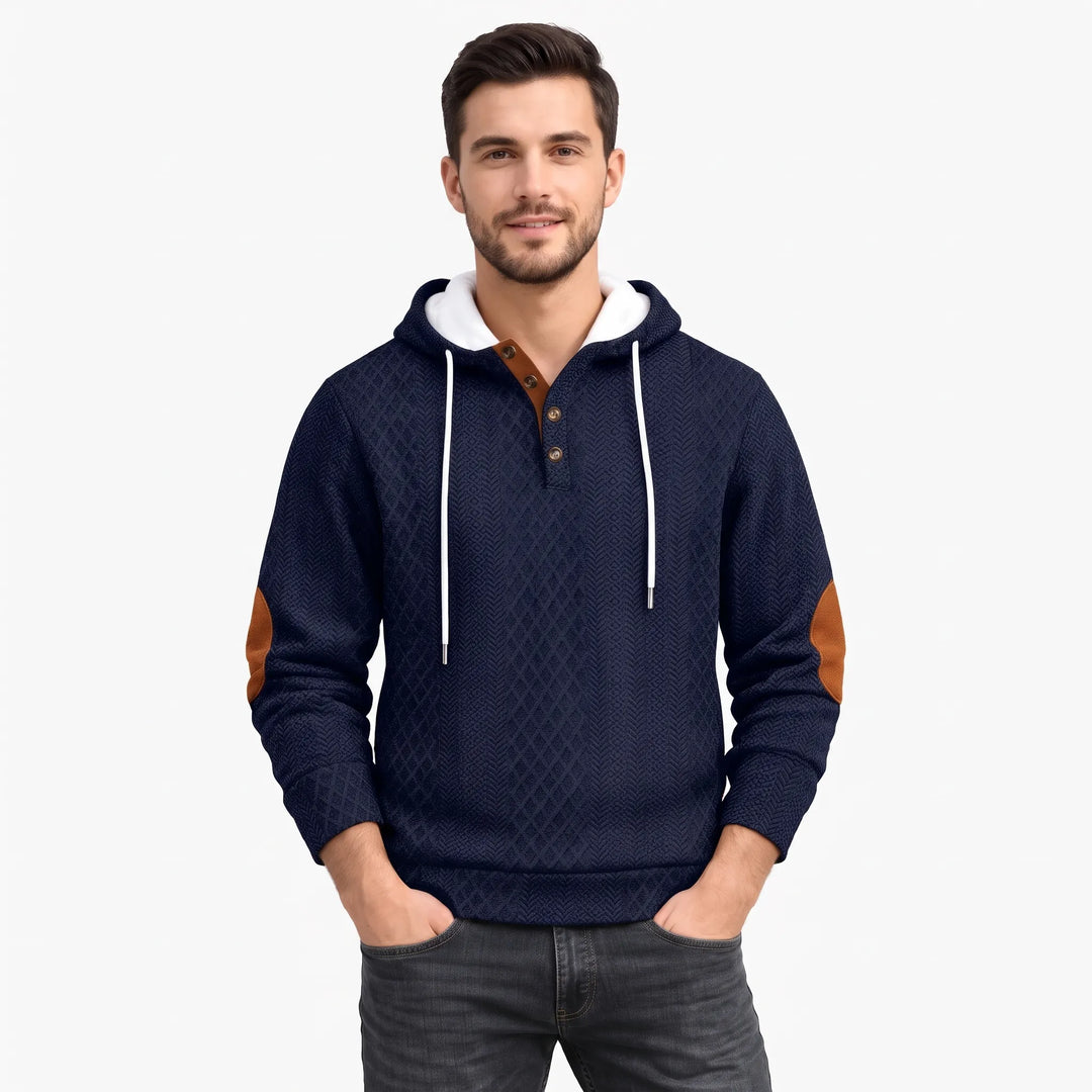 Man in a navy textured hoodie with diamond pattern, brown elbow patches and button placket, hands in pockets 1