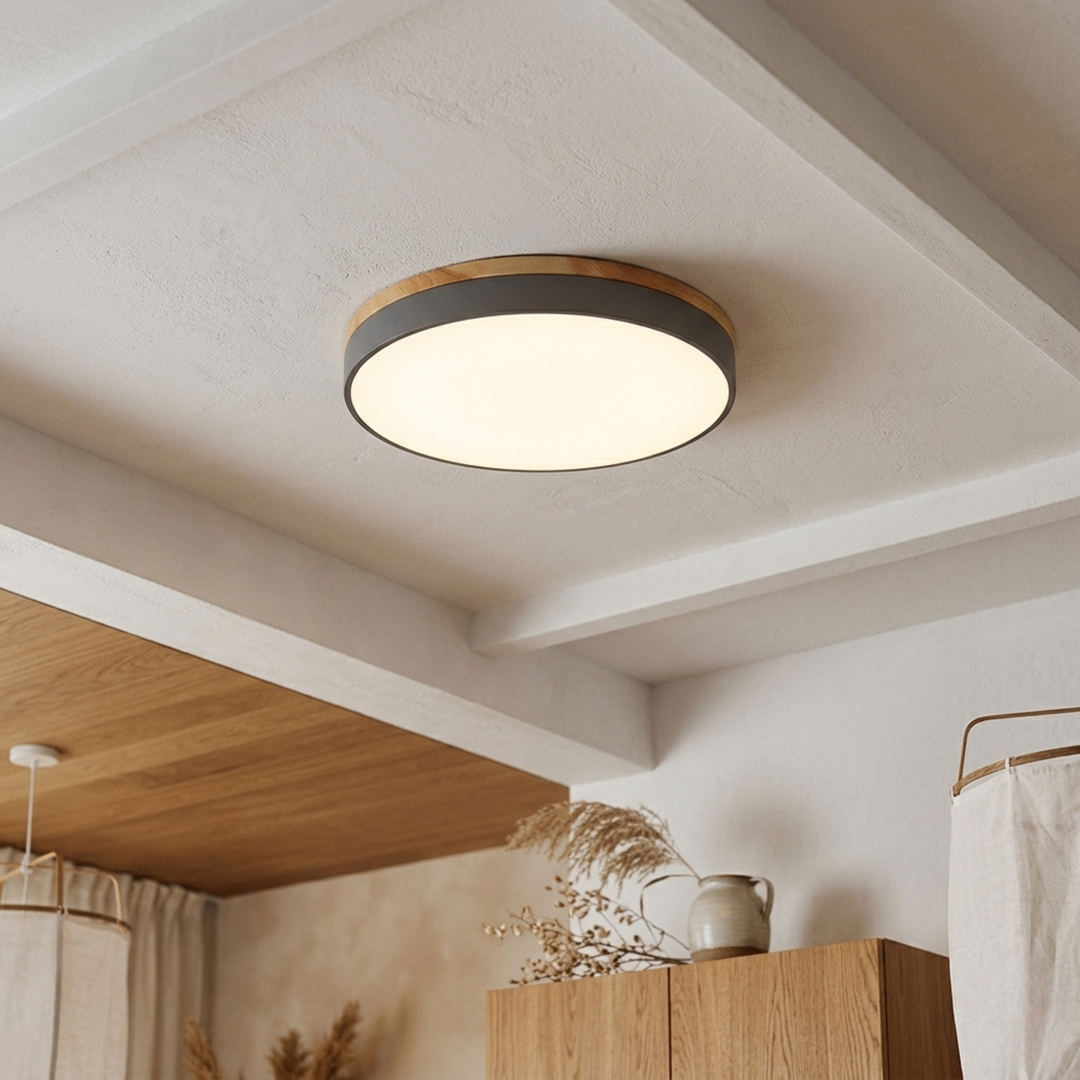 Gray flush-mount disc light with wood-look top trim glowing warm white on a beamed plaster ceiling above wooden cabinets. 9
