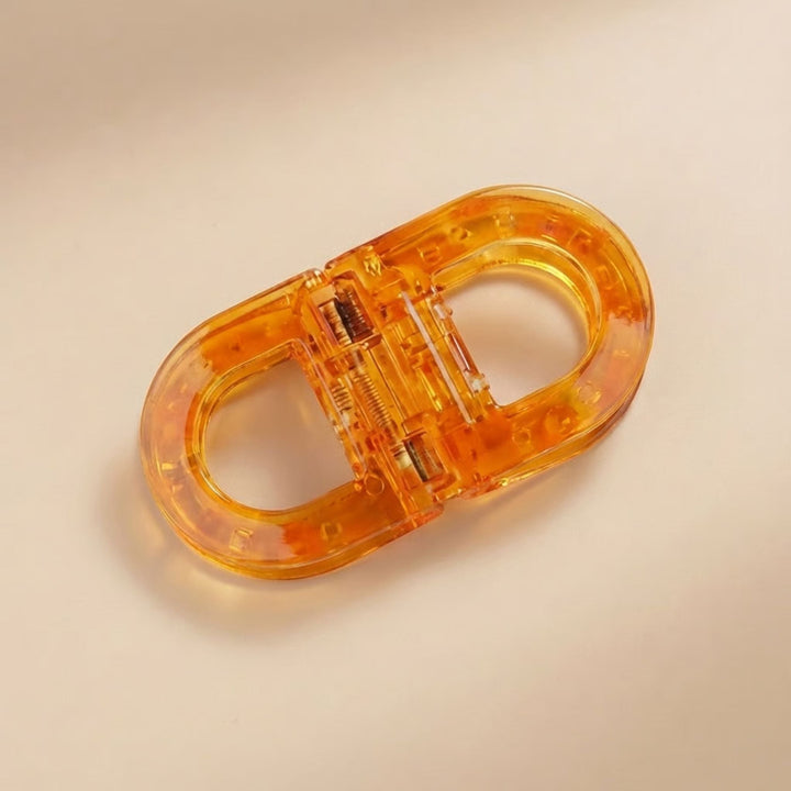 Flat Grip Magnetic Hair Clip in amber-orange, shown open on a beige surface.