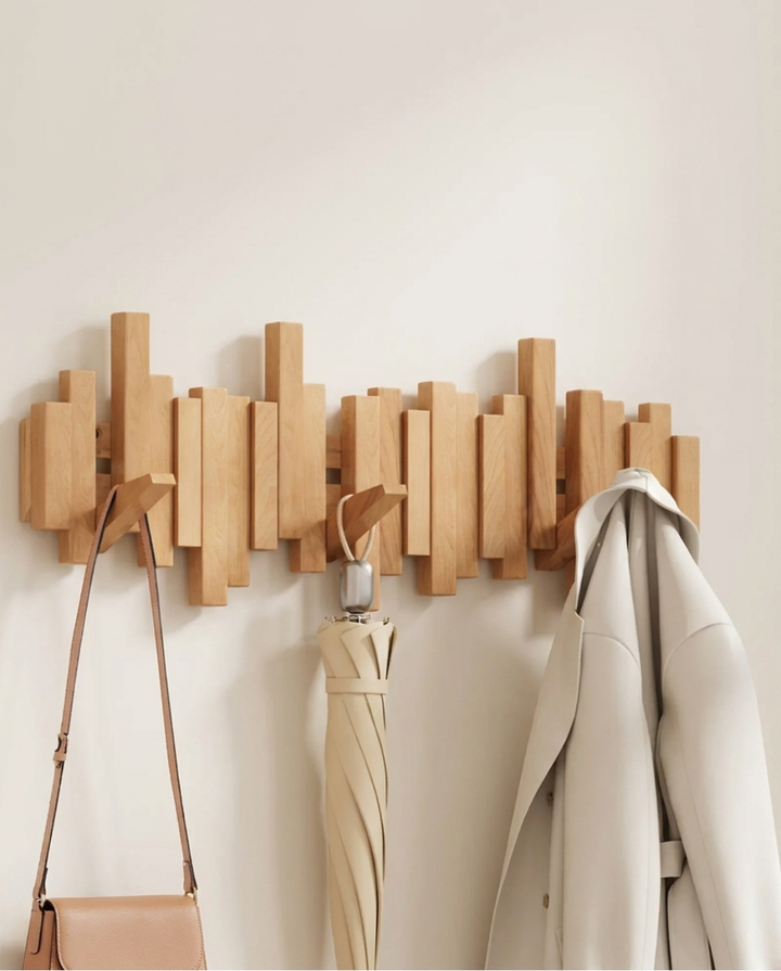 Light natural beech version of the wooden staggered-bar rack, with a tan leather bag, a beige umbrella and a cream coat hanging from its hooks.