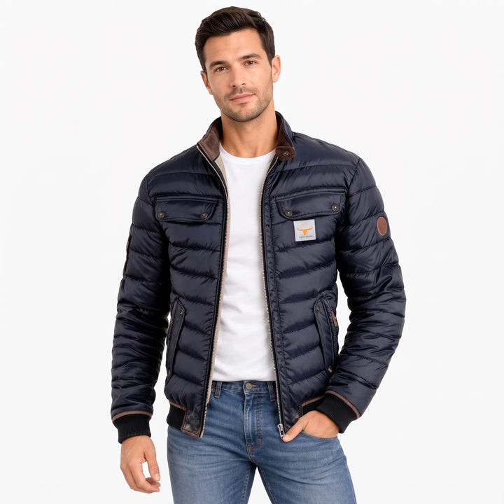 Man wearing the navy quilted jacket unzipped over a white tee and jeans, hand in pocket 1