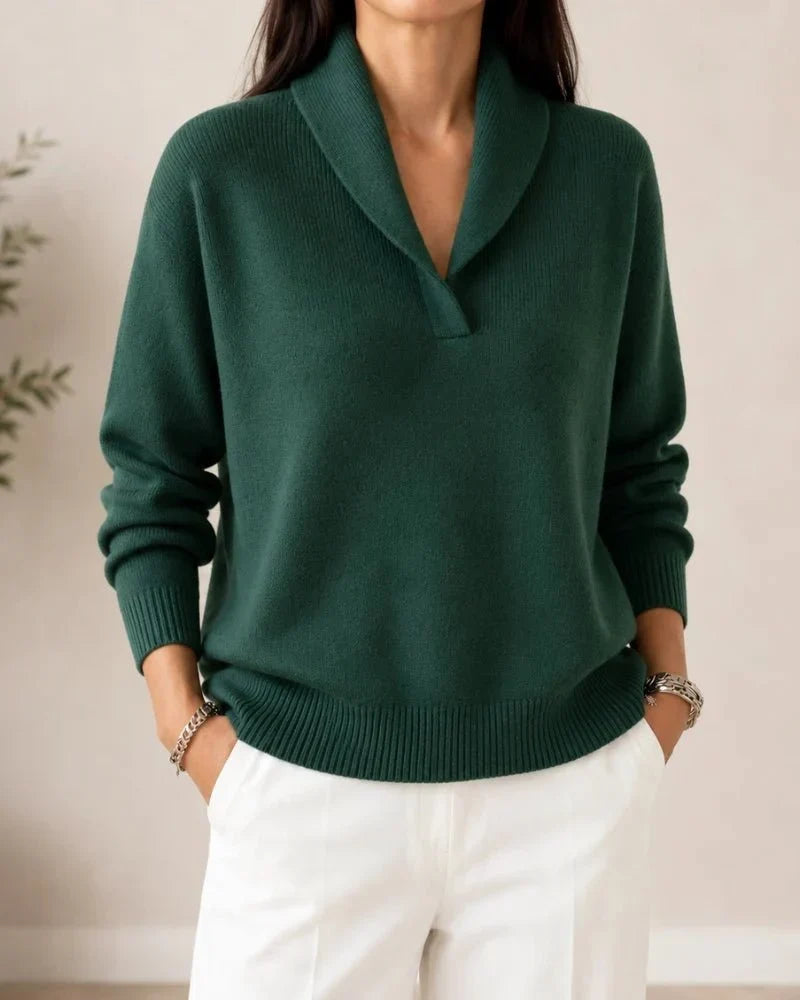 Front view of the dark green ribbed-trim sweater worn by a model with white pants, hands in pockets. 2