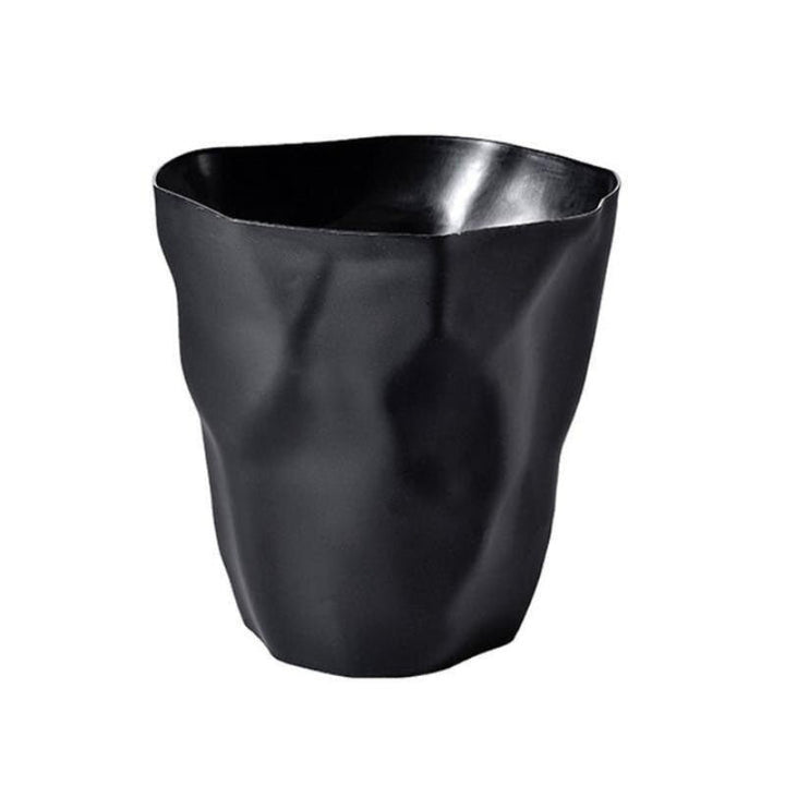 Black wastebasket with a sculptural crumpled paper design and irregular wavy rim.