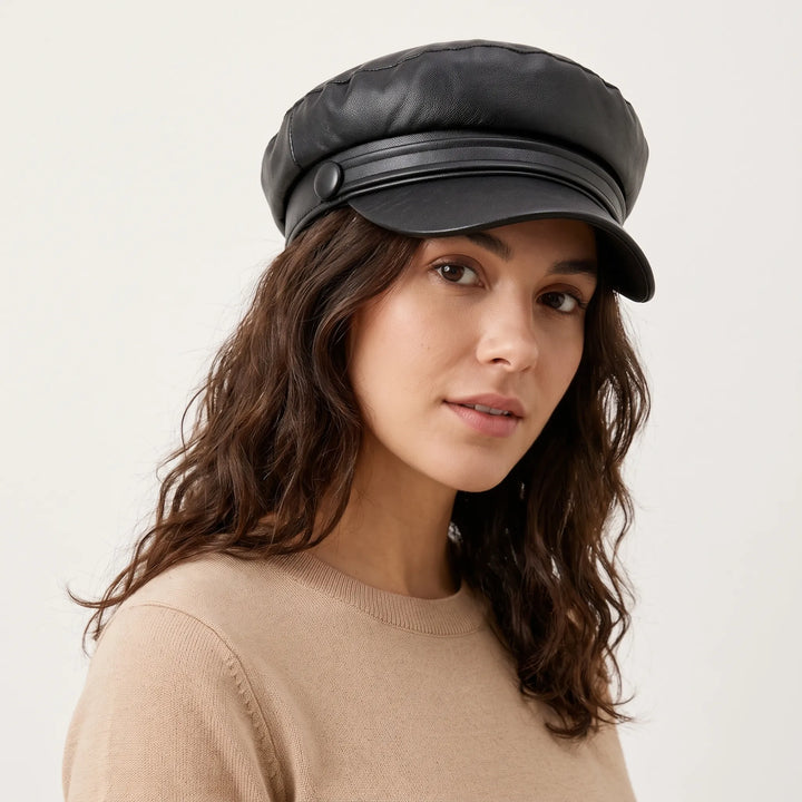 Woman with wavy brown hair wearing the black leather-look cap with button strap, turned slightly to the side 1