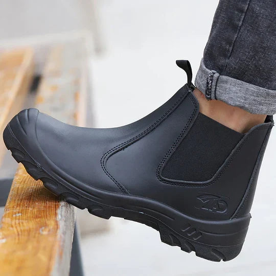 Side view of a black leather slip-on boot worn with rolled gray jeans, foot resting on a wooden step 1