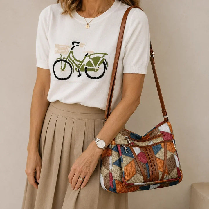 Woman in a white knit tee and beige pleated skirt carries the patchwork bag on her shoulder by its brown strap. 1