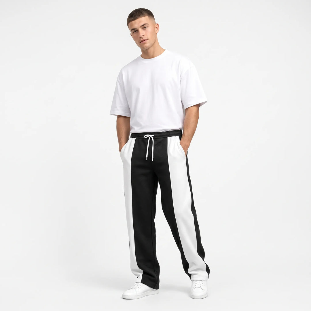 Model in black and white color-block sweatpants with hands in pockets, white tee and sneakers 1