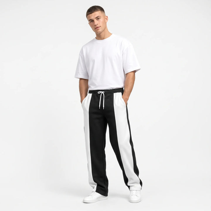 Model in black and white color-block sweatpants with hands in pockets, white tee and sneakers 1