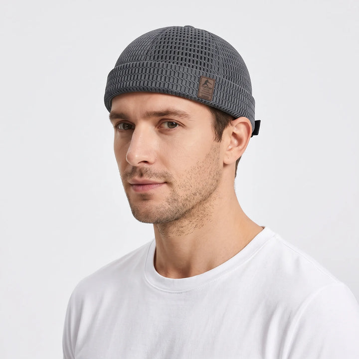 Man in a white t-shirt wearing a gray open weave brimless cap, seen from the side 1