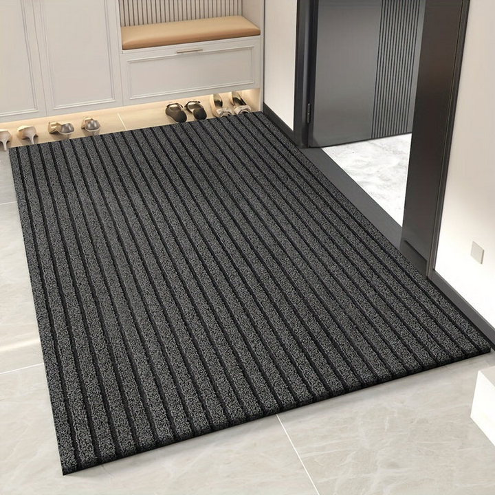 Grey striped doormat with a looped texture in an entryway on a pale tile floor beside a shoe cabinet.