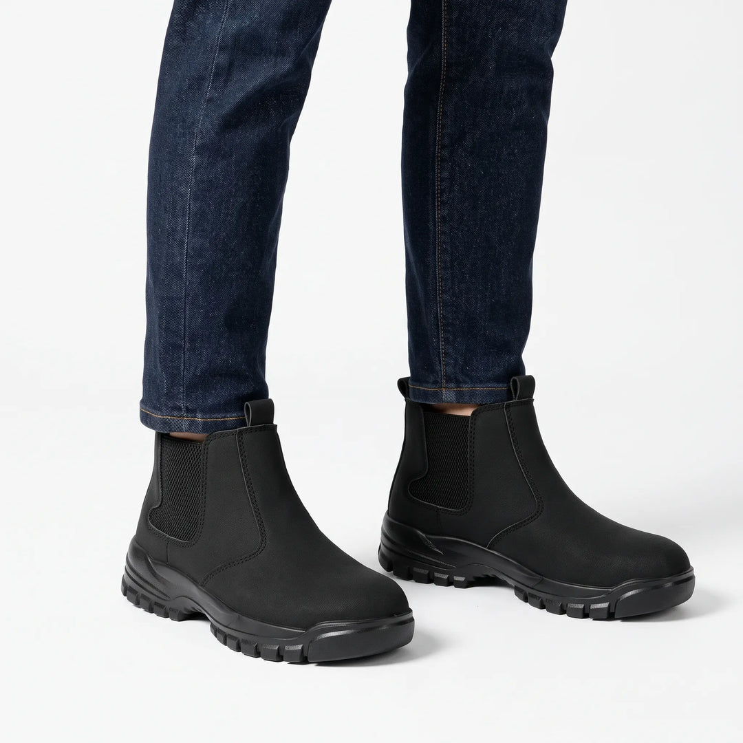 Black slip-on boots with elastic side panels worn with dark blue jeans on a white background 1