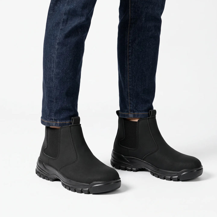 Black slip-on boots with elastic side panels worn with dark blue jeans on a white background 1