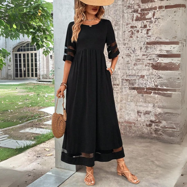 Black maxi dress with sheer-striped sleeves and hem, worn with a straw hat, woven round bag and strappy sandals outdoors. 1