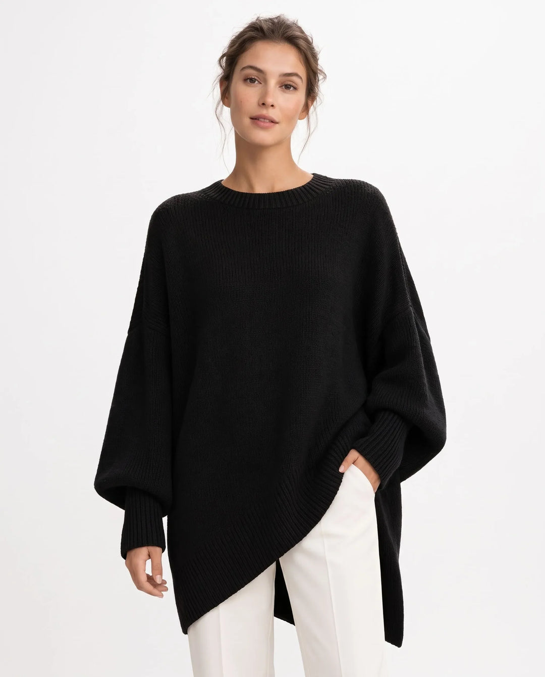 Woman in black oversized knit sweater with ribbed hem and cuffs, white pants, plain studio backdrop 1
